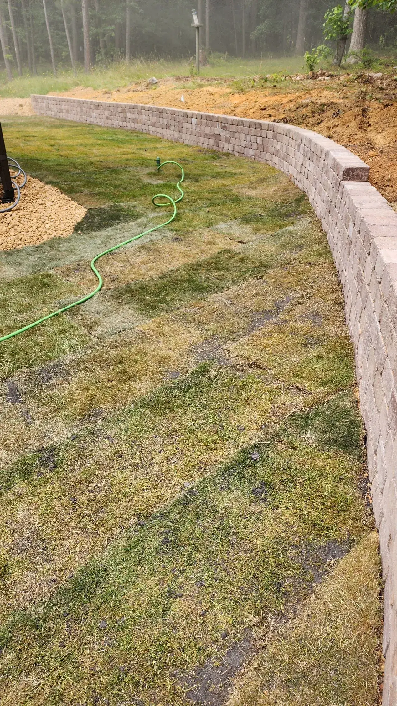 Low brick retaining wall curves along a grassy area, trees in the background.