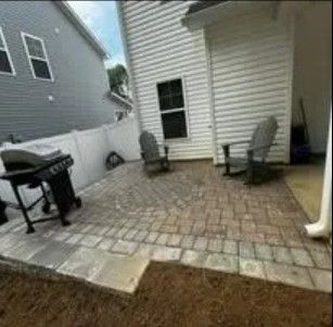 Paver patio with a grill and two Adirondack chairs behind a two-story home with vinyl siding