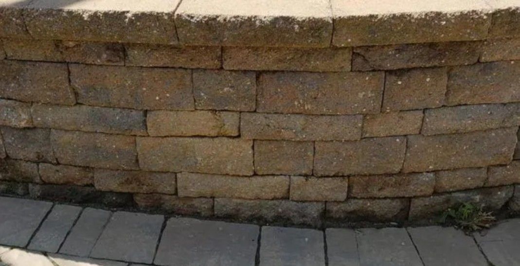 Curved tan block seat wall with a cap row edging a gray paver patio
