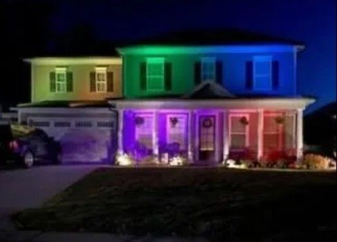 Two-story house lit at night with green, blue, purple and red LED facade lighting