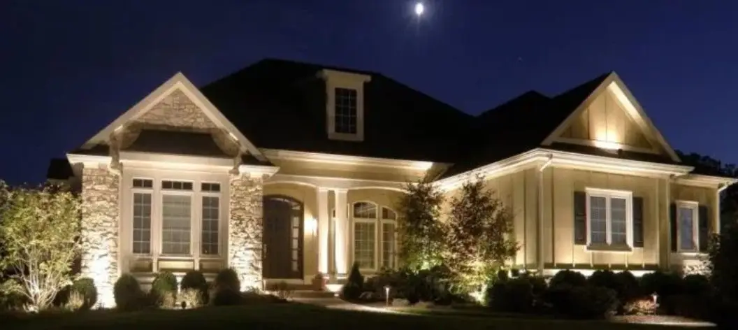 Two-story home at night with warm landscape lighting washing the stone, columns and front beds