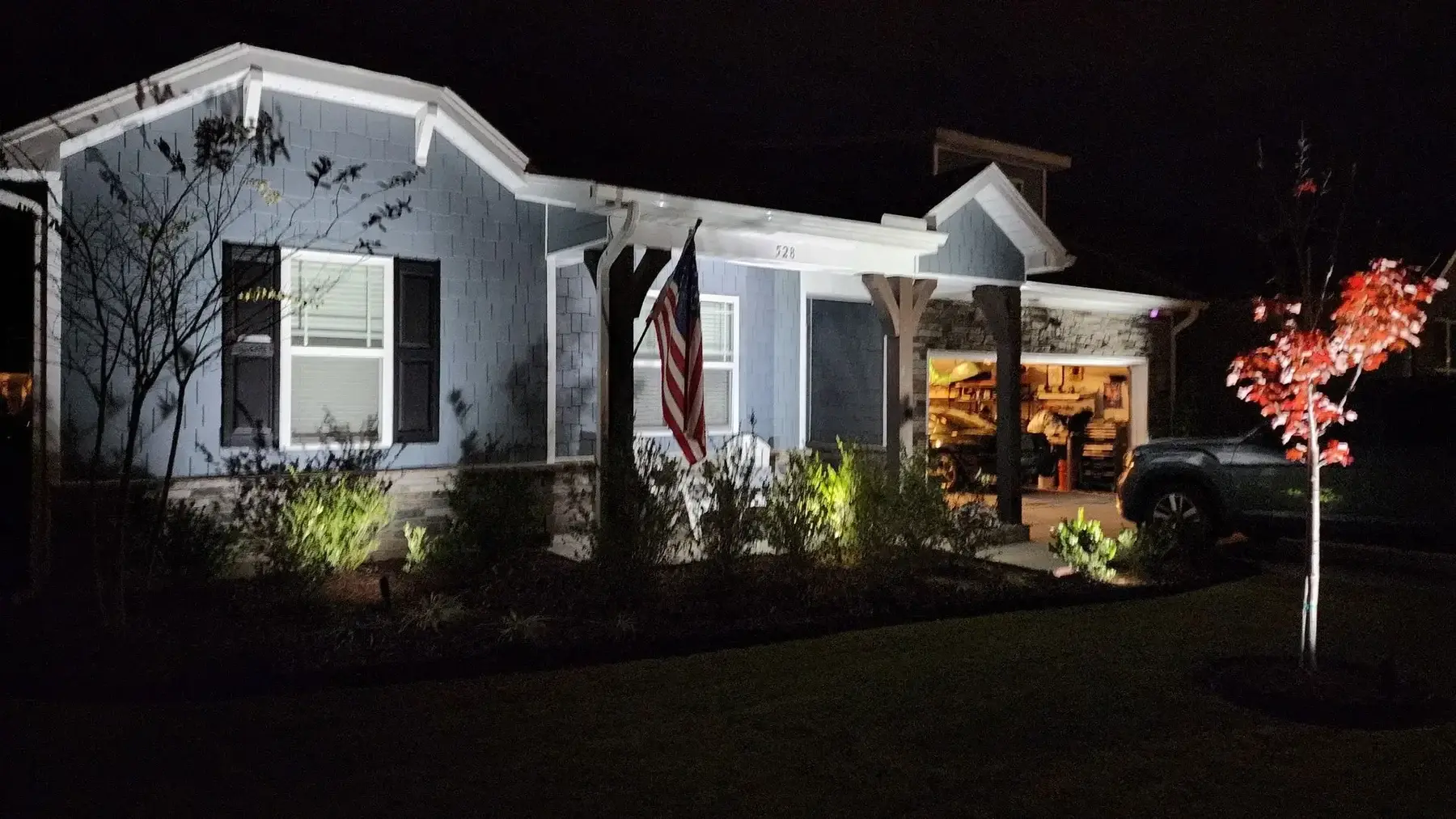 Home at night with landscape lighting on the front beds and an up-lit maple beside the porch