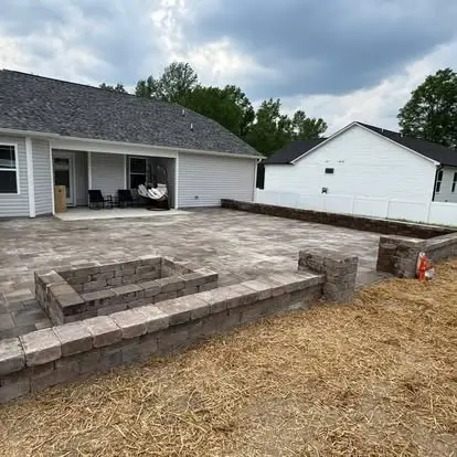 Paver patio with a square fire pit and block seat walls behind a home