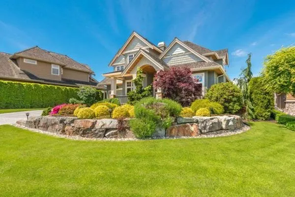 Front lawn and stone-edged planting bed with shrubs in front of a two-story home